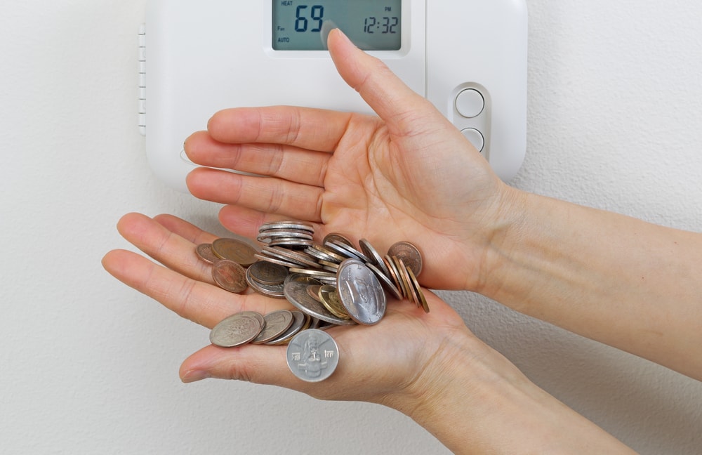woman holding tons of change in her hand in front of thermostat